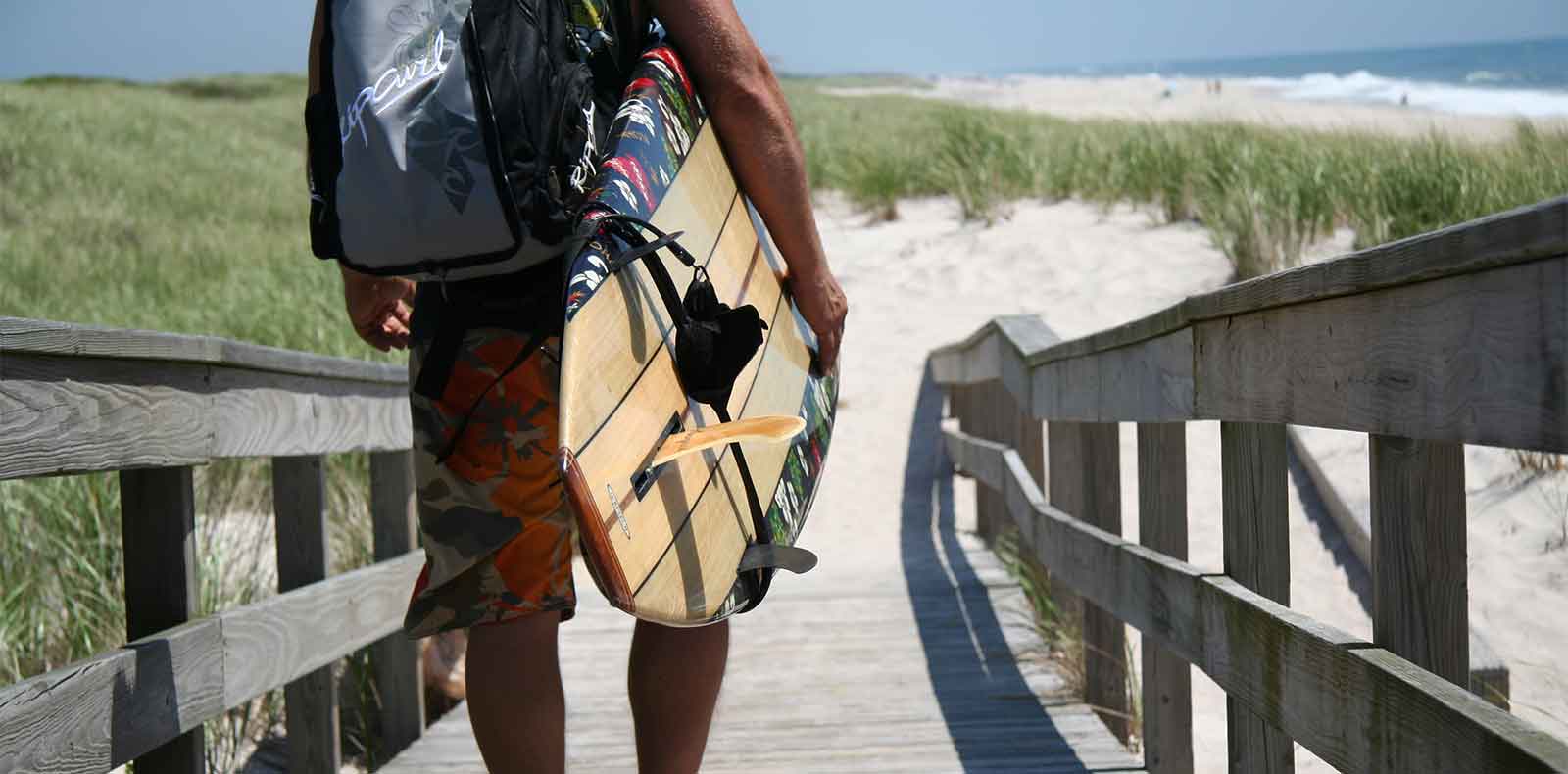 Walking over a wooden bridge to the beach with a surfboard